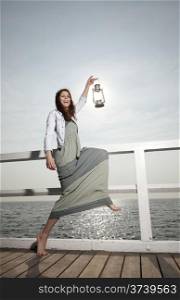 Full length young woman on pier with a oil kerosene lamp. Concept carrying light, daylight
