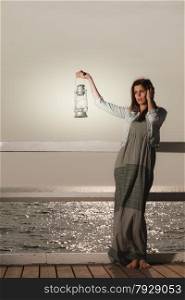Full length young woman on pier with oil kerosene lamp. Concept carrying light, daylight