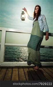 Full length young woman on pier with oil kerosene lamp. Concept carrying light, daylight