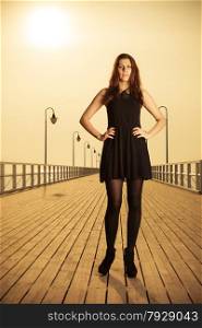 Full length young woman wearing black dress posing on pier in the morning at sunrise