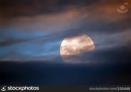 Full moon closeup behind the dark clouds out of focus in the night sky.. Full Moon Behind Clouds