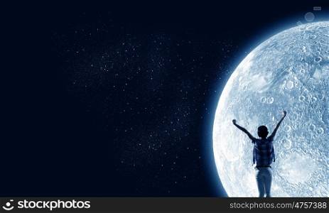 Full moon. Rear view of young woman with hands up looking at moon in sky
