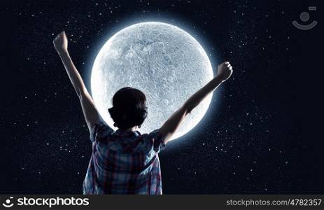 Full moon. Rear view of young woman with hands up looking at moon in sky