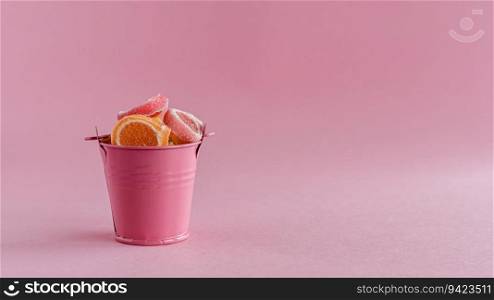 Full of colourful fruit Jelly candy in a pink bucket against pink background for food and snack concept