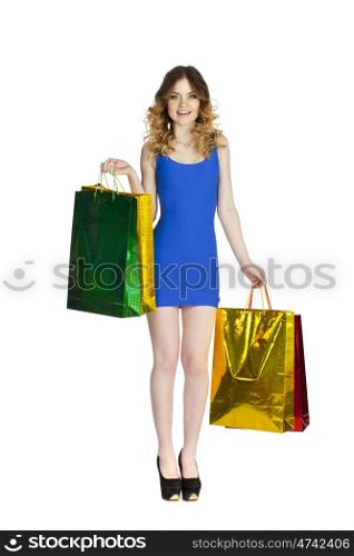 Full portrait of smiling young blonde girl with colorful shopping bags in blue dress posing on a white background