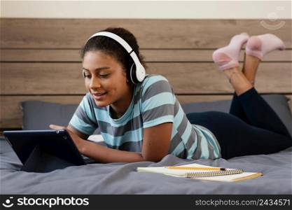 full shot girl with tablet headphones bed