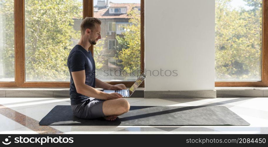 full shot man sitting yoga mat with laptop