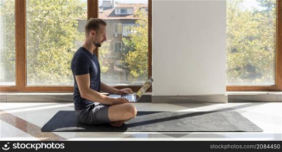 full shot man sitting yoga mat with laptop