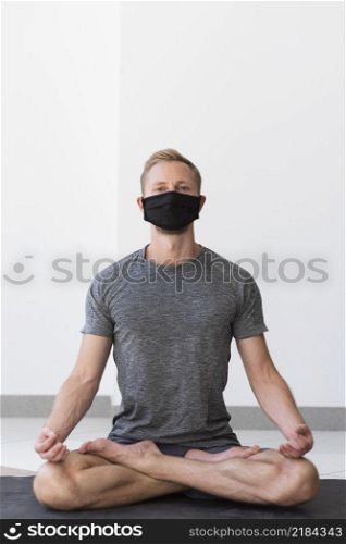 full shot man with face mask doing sukhasana pose inside mat