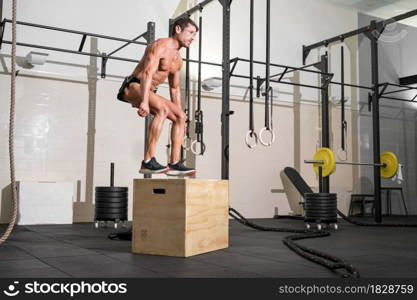Full shot of a fit young caucasian sportsman training alone doing box jump exercise in the gym. High quality photo.. Full shot of a fit young caucasian sportsman training alone doing box jump exercise in the gym.