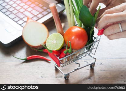 Full with fresh vegetables supermarket shopping cart and laptop in background, Online shopping concept