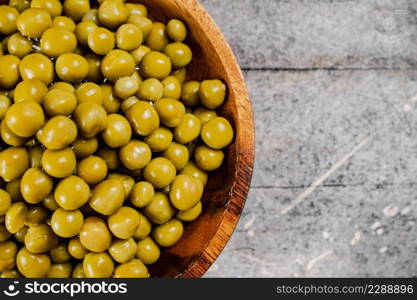 Full wooden plate with canned green peas. On a gray background. High quality photo. Full wooden plate with canned green peas.