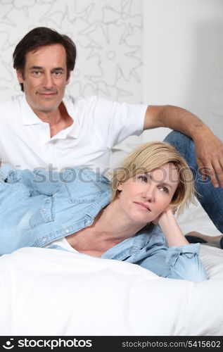 Fully clothed couple lying on a bed watching television