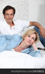 Fully clothed couple lying on a bed watching television
