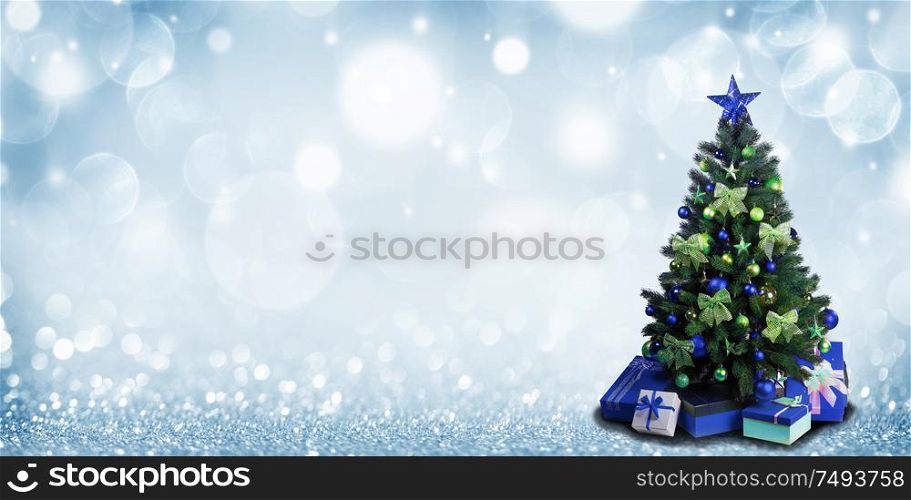 Fully decorated christmas tree with blue and green baubles and bows and presents on glitter bokeh background. Christmas tree with presents