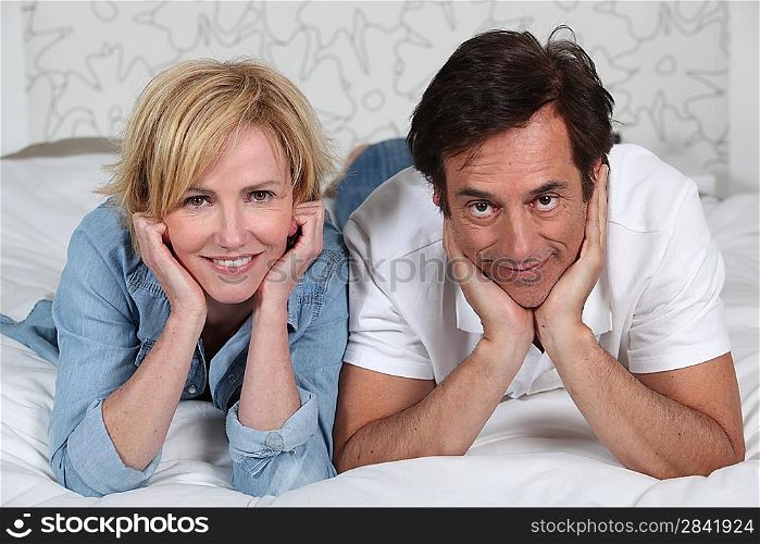 Fully dressed couple lying on a bed watching TV