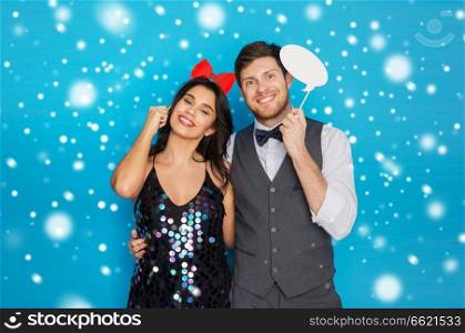 fun and holidays concept - happy couple posing with party props over blue background and snow. happy couple with party props having fun