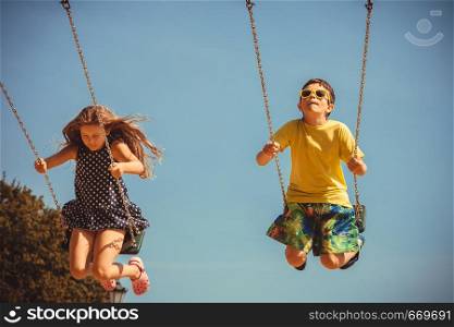 Fun and joy of children. Little girl and boy playing outdoor on preschool playground garden. Kids swinging on swing-set to touch the sky.. Two children having fun on swingset.