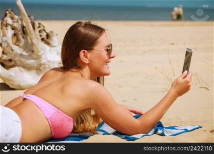 Fun and joy. Summer time. Young beauty girl spending time on beach taking selfie photo by mobile phone. Positive woman with smartphone lying on blanket.. Happy girl taking selfie photo on beach.