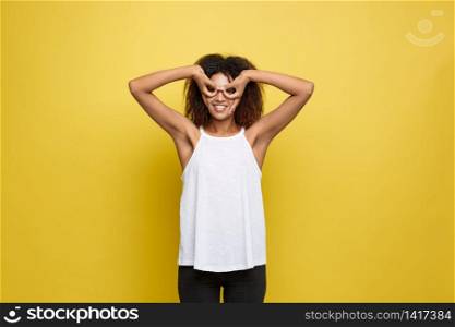 Fun and People Concept - Headshot Portrait of happy Alfo African American woman with freckles smiling and making finger glasses. Pastel yellow studio background. Copy Space. Fun and People Concept - Headshot Portrait of happy Alfo African American woman with freckles smiling and making finger glasses. Pastel yellow studio background. Copy Space.