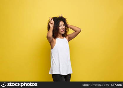 Fun and People Concept - Headshot Portrait of happy Alfo African American woman with freckles smiling and showing rabbit ears with fingers over head . Pastel yellow studio background. Copy Space. Fun and People Concept - Headshot Portrait of happy Alfo African American woman with freckles smiling and showing rabbit ears with fingers over head . Pastel yellow studio background. Copy Space.