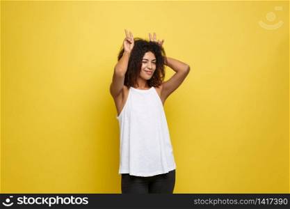 Fun and People Concept - Headshot Portrait of happy Alfo African American woman with freckles smiling and showing rabbit ears with fingers over head . Pastel yellow studio background. Copy Space. Fun and People Concept - Headshot Portrait of happy Alfo African American woman with freckles smiling and showing rabbit ears with fingers over head . Pastel yellow studio background. Copy Space.