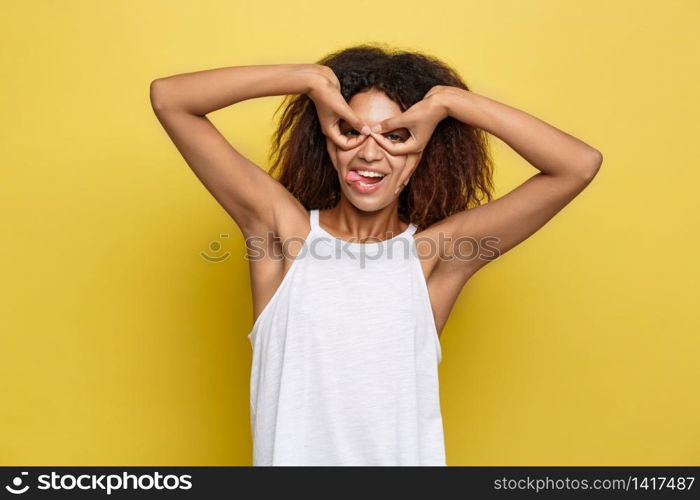 Fun and People Concept - Headshot Portrait of happy Alfo African American woman with freckles smiling and making finger glasses. Pastel yellow studio background. Copy Space. Fun and People Concept - Headshot Portrait of happy Alfo African American woman with freckles smiling and making finger glasses. Pastel yellow studio background. Copy Space.