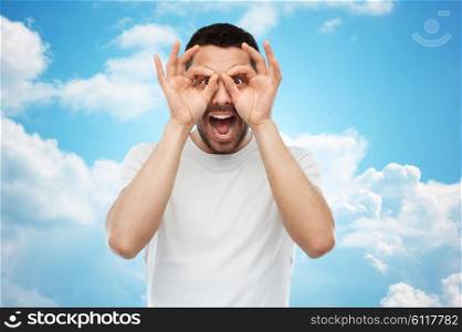 fun and people concept - man making finger glasses over blue sky and clouds background. man making finger glasses over blue sky
