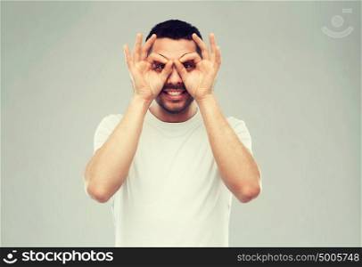 fun and people concept - man making finger glasses over gray background. man making finger glasses over gray background