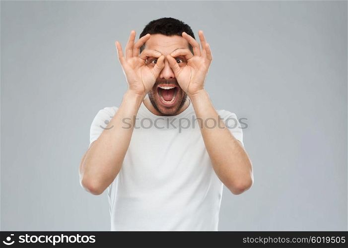 fun and people concept - man making finger glasses over gray background. man making finger glasses over gray background
