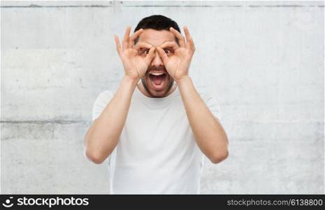 fun and people concept - man making finger glasses over gray stone wall background. man making finger glasses over gray background