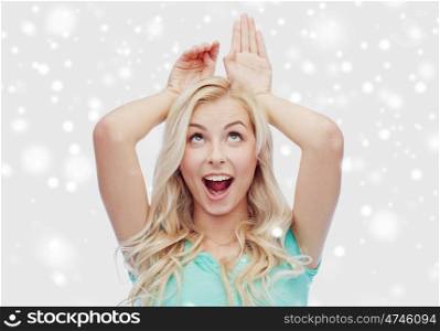 fun, christmas, winter holidays and people concept - happy smiling young woman making bunny ears over snow
