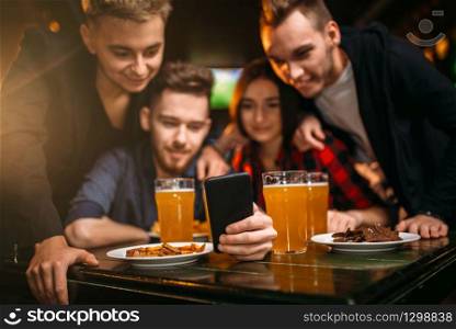 Fun company watches photo on phone in a sport bar, happy football fans. Fun company watches photo on phone in a sport bar