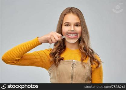 fun, dental care and people concept - happy teenage girl showing her teeth through magnifying glass over grey background. teenage girl shows teeth through magnifying glass
