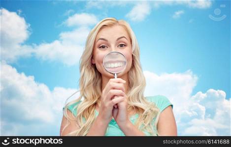 fun, emotions, expressions and people concept - happy smiling young woman or teenage girl having fun with magnifying glass over blue sky and clouds background