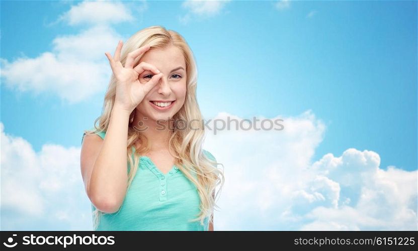 fun, emotions, expressions and people concept - smiling young woman or teenage girl making ok hand gesture over blue sky and clouds background