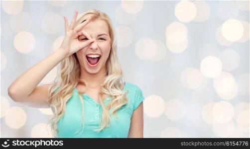 fun, emotions, expressions and people concept - smiling young woman or teenage girl making ok hand gesture over holidays lights background