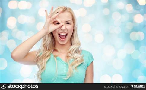 fun, emotions, expressions and people concept - smiling young woman or teenage girl making ok hand gesture over blue holidays lights background