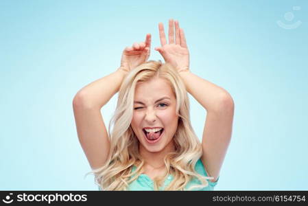 fun, expressions, easter and people concept - happy smiling young woman making bunny ears over blue background