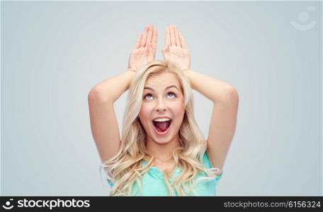 fun, expressions, easter and people concept - happy smiling young woman making bunny ears over gray background
