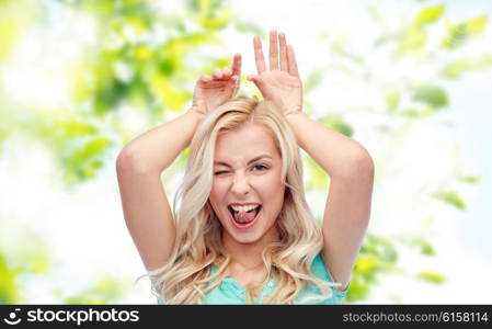 fun, expressions, easter and people concept - happy smiling young woman making bunny ears over green natural background