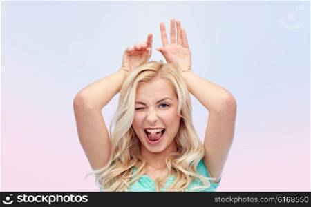fun, expressions, easter and people concept - happy smiling young woman making bunny ears over rose quartz and serenity gradient background
