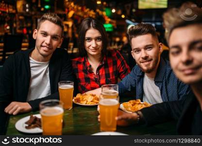 Fun friends sitting at the table with beer and crisps in a sport bar, happy leisure of football fans