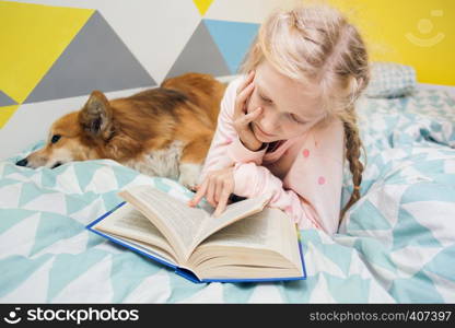 fun girl and dog corgi on the bed in the nursery play on the tablet. home schooling