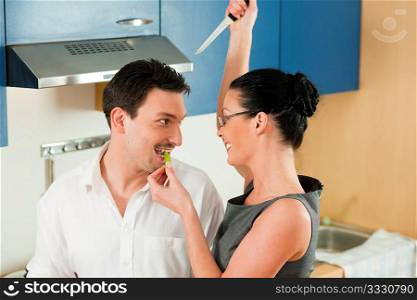 Fun in the kitchen ? woman is holding a knife over the head of her husband