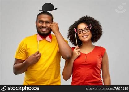 fun, photo booth and people concept - happy african american couple with party props over grey background. happy african american couple with party props
