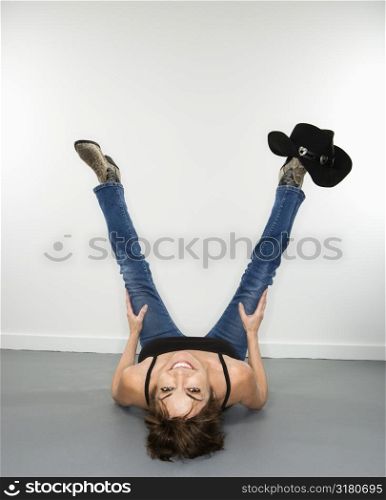 Fun portrait of smiling pretty Caucasian woman lying on back looking upside down with cowboy hat on foot.