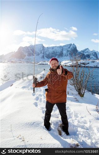fun unsuccessful fishing. smiling man with fishing rod and tangled fishing line on the background of the ocean and mountains. Lofoten Islands. Norway.