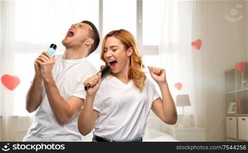 fun, valentine&rsquo;s day and people concept - portrait of happy couple in white t-shirts couple singing to hairbrush and lotion bottle over home bedroom decorated with heart shaped balloons background. happy couple singing to hairbrush and lotion