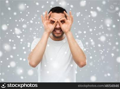 fun, winter, christmas and people concept - man making finger glasses over snow on gray background
